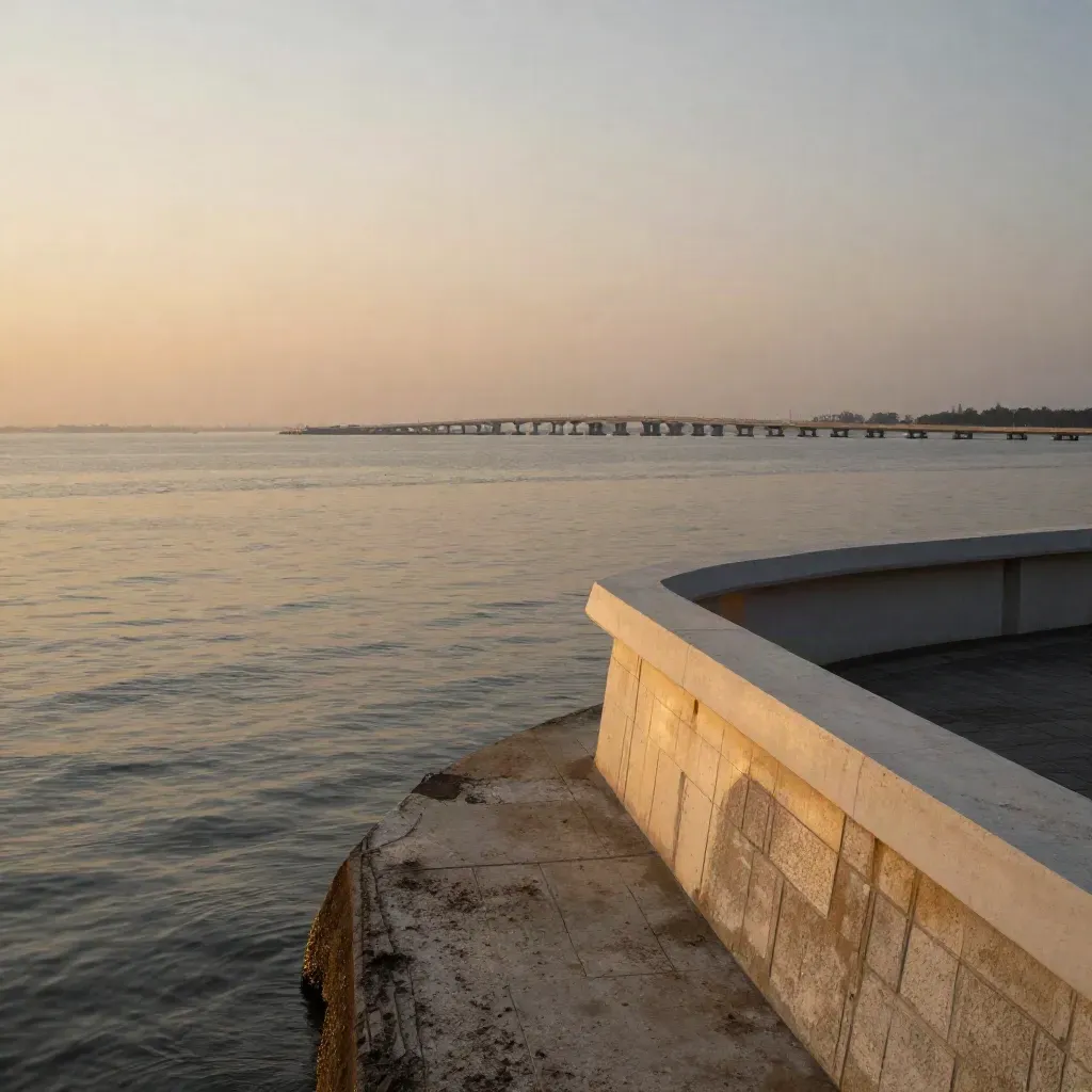 Pemandangan pesisir Johor Bahru dengan jambatan, skyline rendah dan laut berkilau waktu senja.